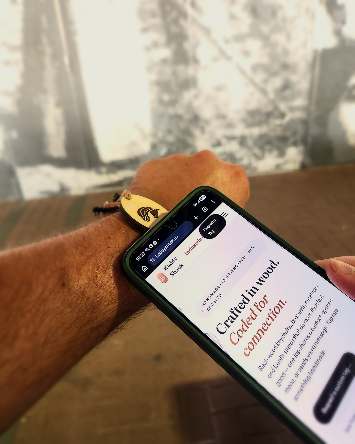 Wood NFC bracelet with engraved horse logo next to a phone showing the Kaddy Shack Industries site